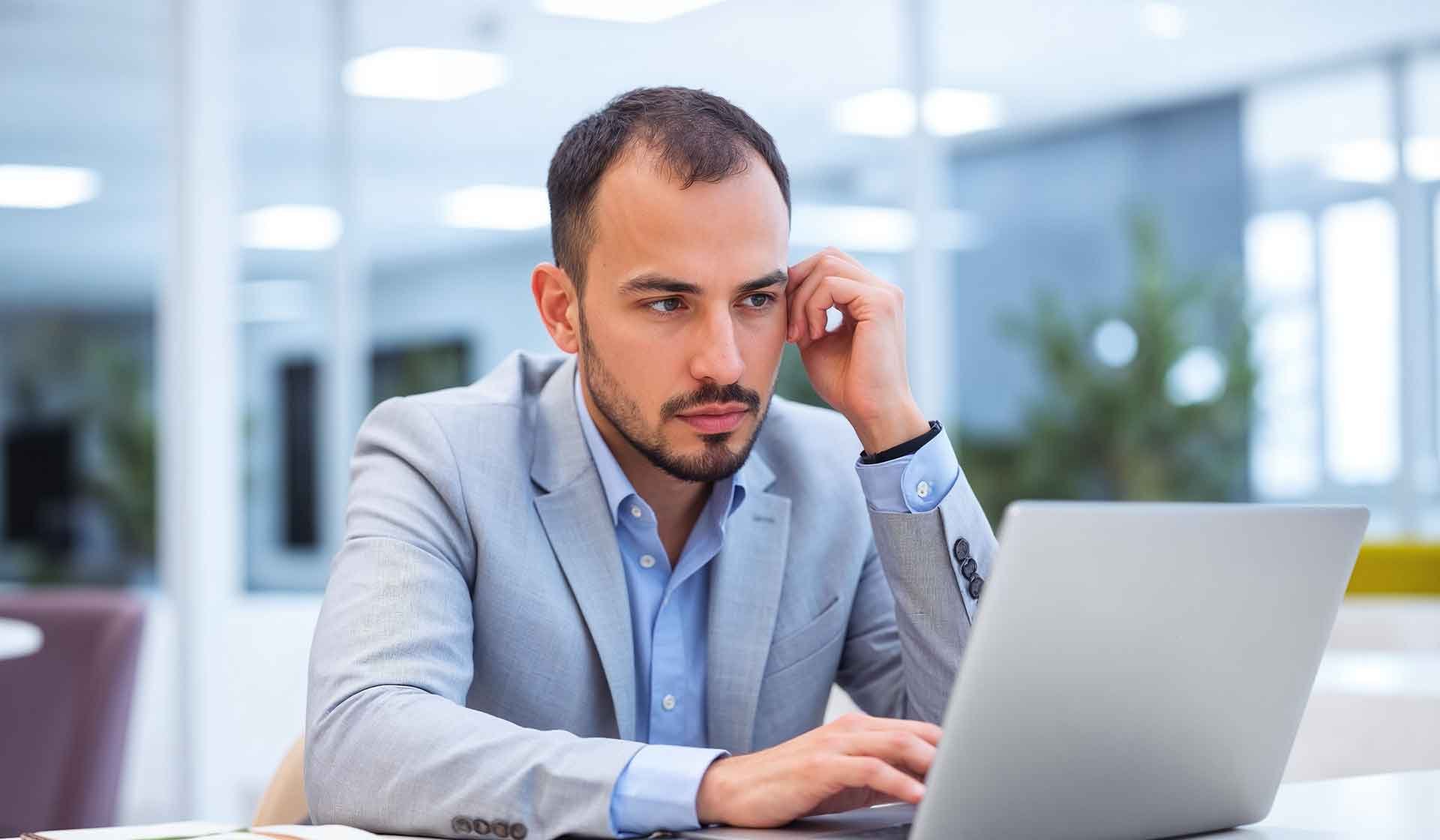 Nachdenklicher Mann im Anzug arbeitet am Laptop im modernen Büro – Symbolbild für die Auseinandersetzung mit rechtlichen Vorschriften wie der Entgeltbescheinigungsverordnung