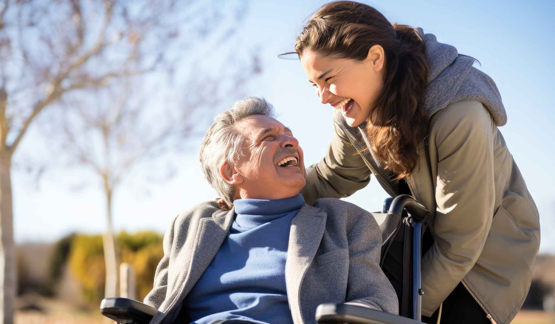 Junge Frau lacht mit einem älteren Mann im Rollstuhl bei einem Spaziergang – Symbolbild für Pflege, Unterstützung und zwischenmenschliche Nähe
