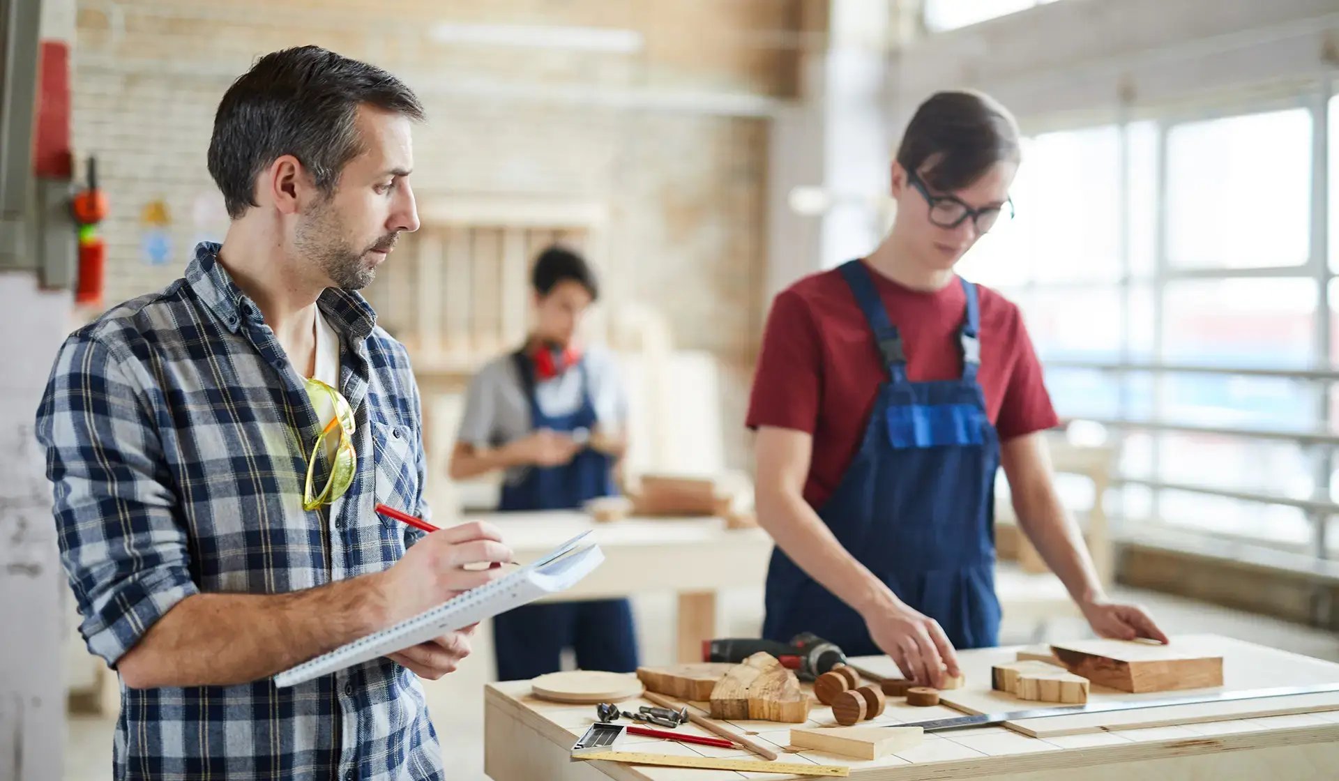 Ausbilder beobachtet jungen Handwerker bei der Holzbearbeitung in einer Werkstatt – Sinnbild für Weiterbildung im Handwerk